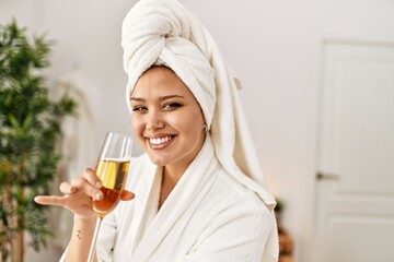 Young beautiful hispanic woman wearing bathrobe drinking champagne at beauty salon