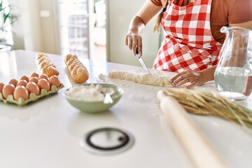 Young beautiful hispanic woman making bread at the kitchen