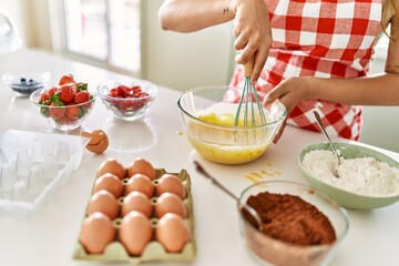 Young beautiful hispanic woman mixing eggs at the kitchen