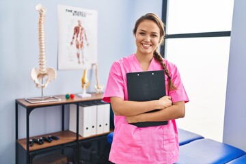 Young beautiful hispanic woman physiotherapist smiling confident holding document at rehab clinic - Powered by Adobe