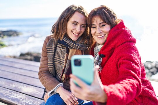 Two women mother and daughter make selfie by smartphone sitting on bench at seaside