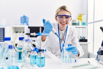 Young blonde woman scientist pouring liquid on test tube at laboratory