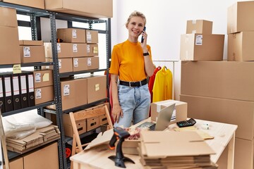 Young blonde woman ecommerce business worker talking on smartphone standing at office