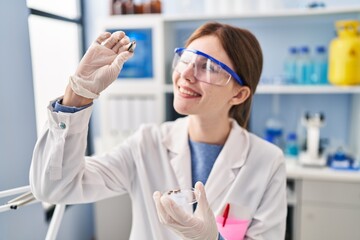 Young blonde woman scientist holding sample with tweezers at laboratory