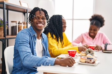 Group of three young black people sitting on a table having coffee looking positive and happy...