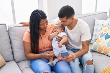 Hispanic family using smartphone sitting on sofa at home