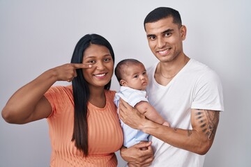 Obraz premium Young hispanic couple with baby standing together over isolated background pointing with hand finger to face and nose, smiling cheerful. beauty concept
