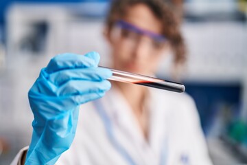 Young hispanic woman scientist holding blood test tube analysis at laboratory