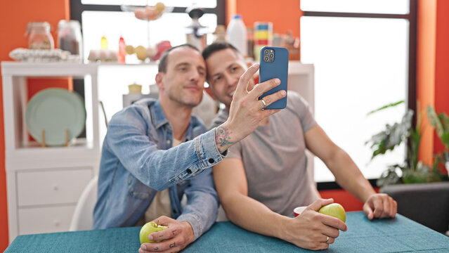 Two men couple make selfie by smartphone holding apple at dinning room