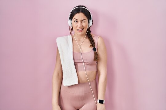 Young brunette woman wearing sportswear and headphones winking looking at the camera with sexy expression, cheerful and happy face.