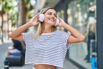 Young blonde woman listening to music and dancing at street