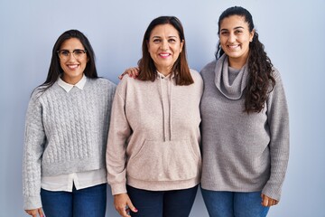 Mother and two daughters standing over blue background with a happy and cool smile on face. lucky...