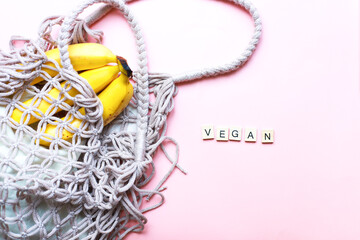 Vegan inscription from wooden letters. Flat lay zero waste shopping bag with fruits on pink...