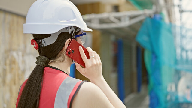 Young beautiful hispanic woman builder talking on smartphone at street