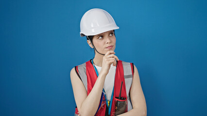 Young beautiful hispanic woman builder standing with doubt expression over isolated blue background