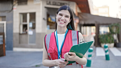 Young beautiful hispanic woman survey interviewer smiling confident holding clipboard at street