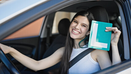 Young beautiful hispanic woman sitting on car holding license of new driver at street