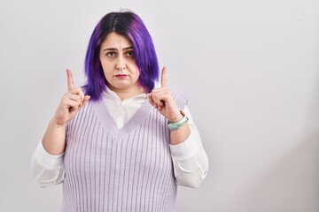 Obraz na płótnie Canvas Plus size woman wit purple hair standing over white background pointing up looking sad and upset, indicating direction with fingers, unhappy and depressed.