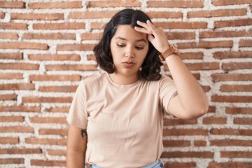 Young hispanic woman standing over bricks wall worried and stressed about a problem with hand on forehead, nervous and anxious for crisis