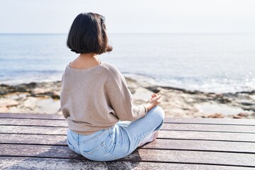 Fototapeta na wymiar Young woman doing yoga exercise sitting on bench at seaside