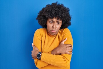 Fototapeta na wymiar Black woman with curly hair standing over blue background shaking and freezing for winter cold with sad and shock expression on face