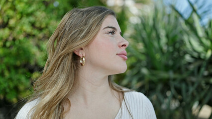Naklejka premium Young blonde woman looking to the side with relaxed expression at park