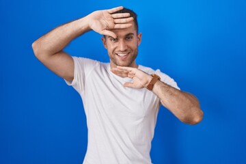 Young caucasian man standing over blue background smiling cheerful playing peek a boo with hands...