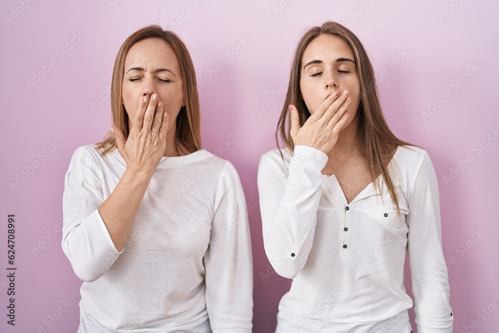 Poster middle age mother and young daughter standing over pink background bored yawning tired covering mout