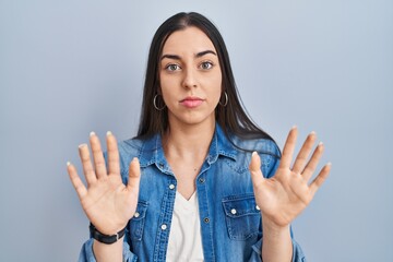 Hispanic woman standing over blue background moving away hands palms showing refusal and denial...