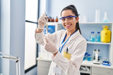 Young beautiful hispanic woman scientist holding plant with tweezer at laboratory
