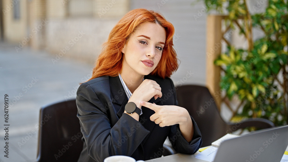 Wall mural Young redhead woman business worker pointing to watch at coffee shop terrace