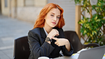 Young redhead woman business worker pointing to watch at coffee shop terrace
