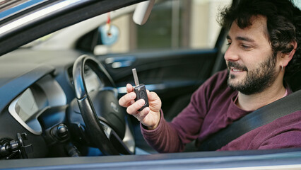 Young hispanic man smiling confident holding key of new car at street