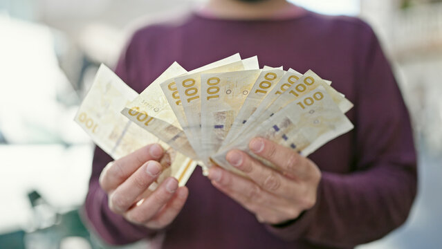 Young hispanic man counting denmark krone banknotes at street