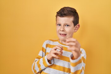 Young caucasian kid standing over yellow background disgusted expression, displeased and fearful doing disgust face because aversion reaction. with hands raised - obrazy, fototapety, plakaty