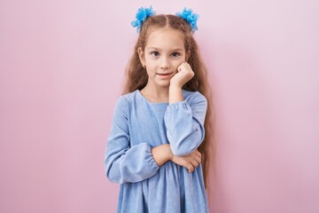 Young little girl standing over pink background looking stressed and nervous with hands on mouth biting nails. anxiety problem.