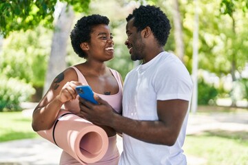 African american man and woman couple holding yoga mat using smartphone at park