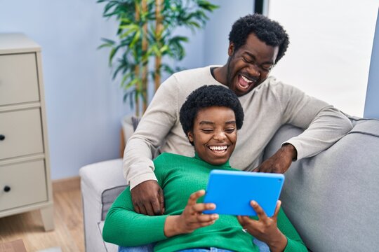 African american man and woman couple using touchpad sitting on sofa at home
