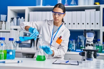 Fototapeta premium Young african american woman scientist pouring liquid at laboratory
