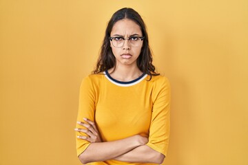 Obraz premium Young brazilian woman wearing glasses over yellow background skeptic and nervous, disapproving expression on face with crossed arms. negative person.