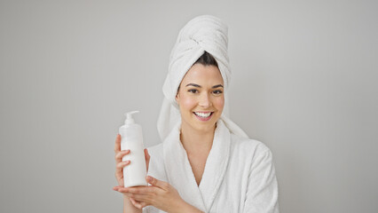 Young beautiful hispanic woman wearing bathrobe holding lotion bottle over isolated white background