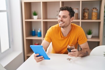 Young hispanic man using touchpad drinkng wine at home