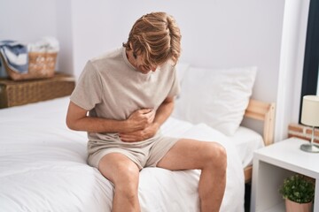 Young man suffering for stomach flu sitting on bed at bedroom