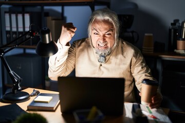 Middle age man with grey hair working at the office at night angry and mad raising fist frustrated...