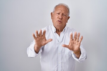 Senior man with grey hair standing over isolated background moving away hands palms showing refusal...