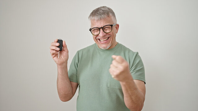 Middle age grey-haired man smiling confident holding key of new car over isolated white background
