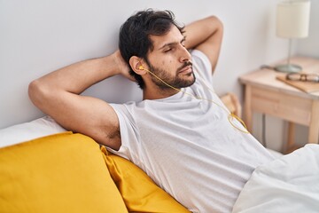 Young hispanic man listening to music relaxed on bed at bedroom