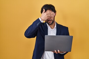 Handsome latin man working using computer laptop covering eyes with hand, looking serious and sad. sightless, hiding and rejection concept