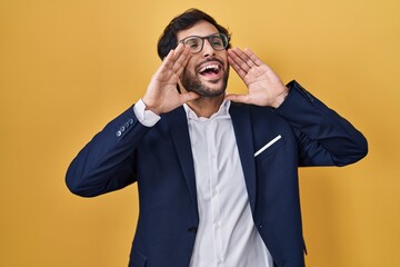 Handsome latin man standing over yellow background smiling cheerful playing peek a boo with hands showing face. surprised and exited