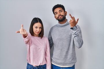 Young hispanic couple standing together showing middle finger, impolite and rude fuck off expression